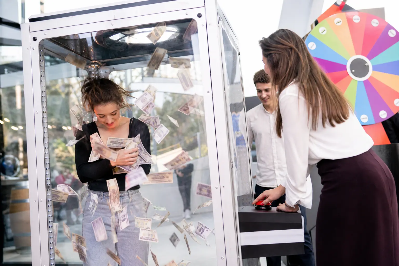 Jeune femme dans une cabine à billets attrapant des billets sous les yeux de participants lors d’une animation événementielle.